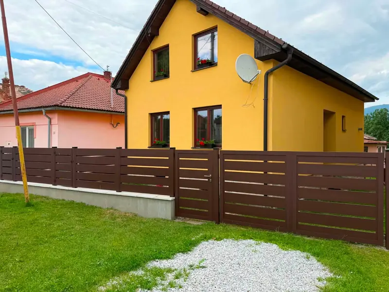 Hnedý hliníkový lamelový plot s bránkou pred rodinným domom