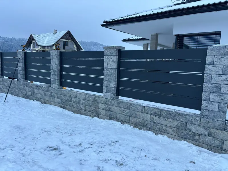 Hliníkové plotové výplne v antracite na murovanom plote v zime pod horami